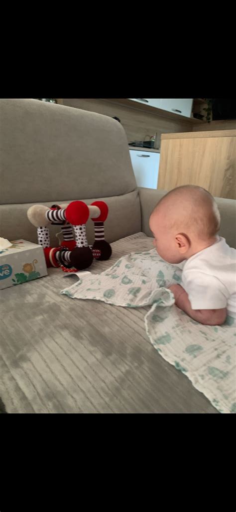 Dojča v polohe na brušku, opierajúce sa o jednu ruku a predlaktie, s druhou rukou voľnou na uchopenie hračky