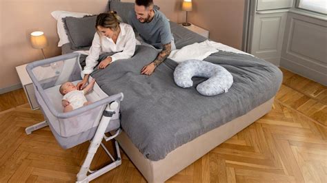 Ilustračná fotografia postieľky Chicco Next2Me v šedej farbe, umiestnenej pri manželskej posteli.