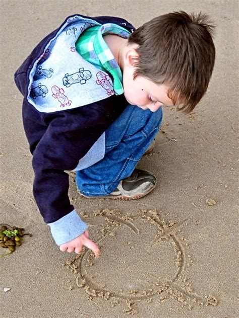 Ilustrácia dieťaťa píšuceho prstom do piesku.